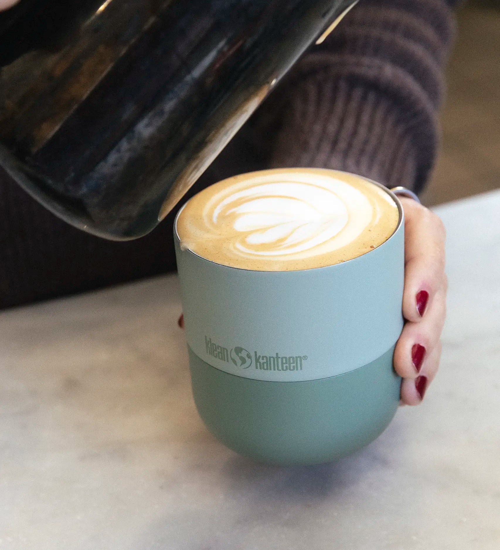 Adult hand holding a Klean Kanteen 8oz iceberg green lowball tumbler filled with coffee