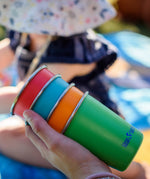 Four cups from the Klean Kanteen Kid cups four in the Beach ball colour way in a hand.