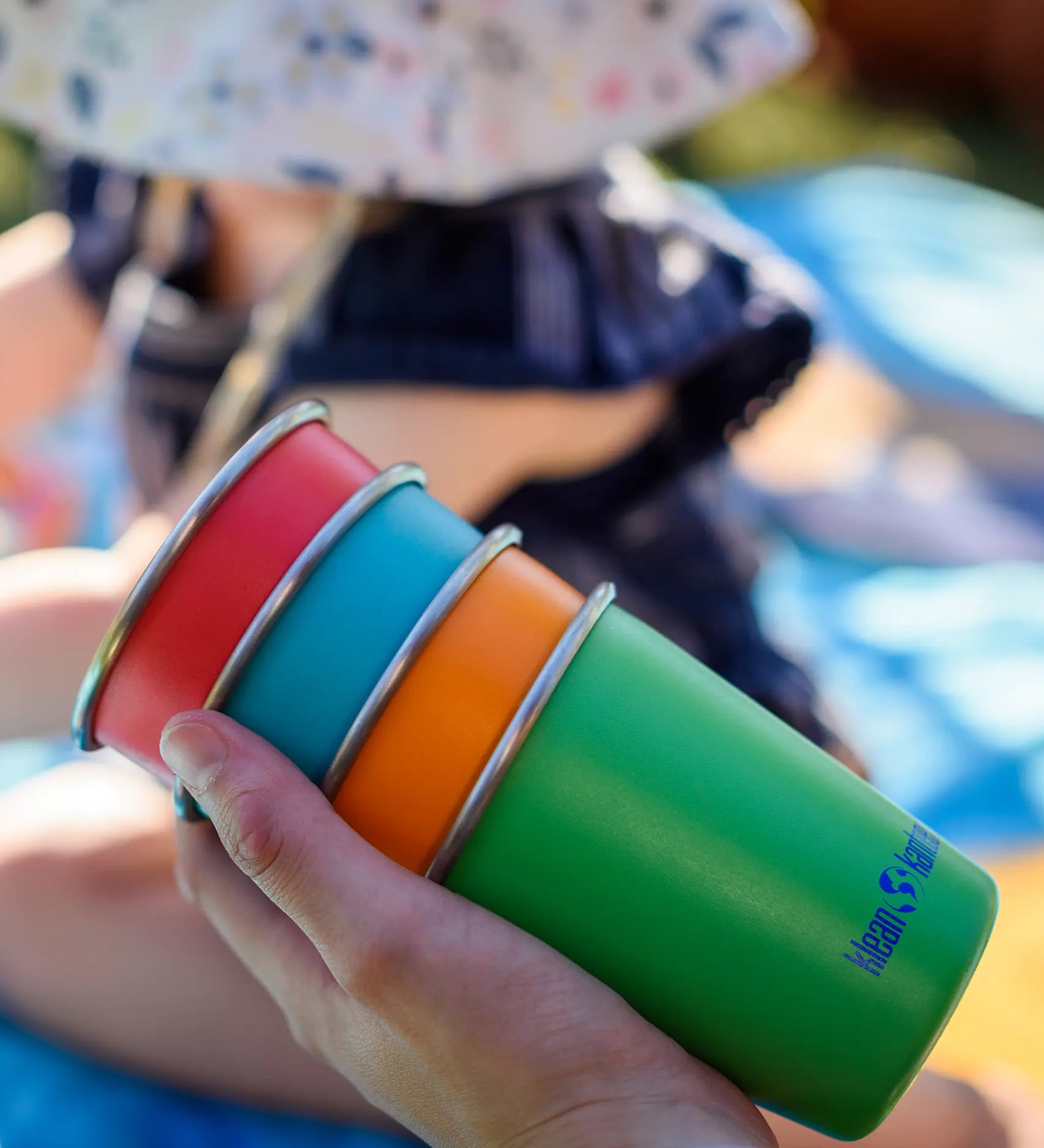 Four cups from the Klean Kanteen Kid cups four in the Beach ball colour way in a hand.