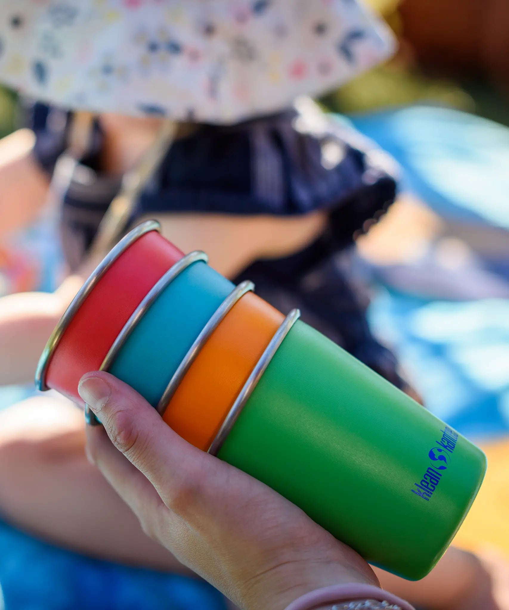 Four cups from the Klean Kanteen Kid cups four in the Beach ball colour way in a hand.