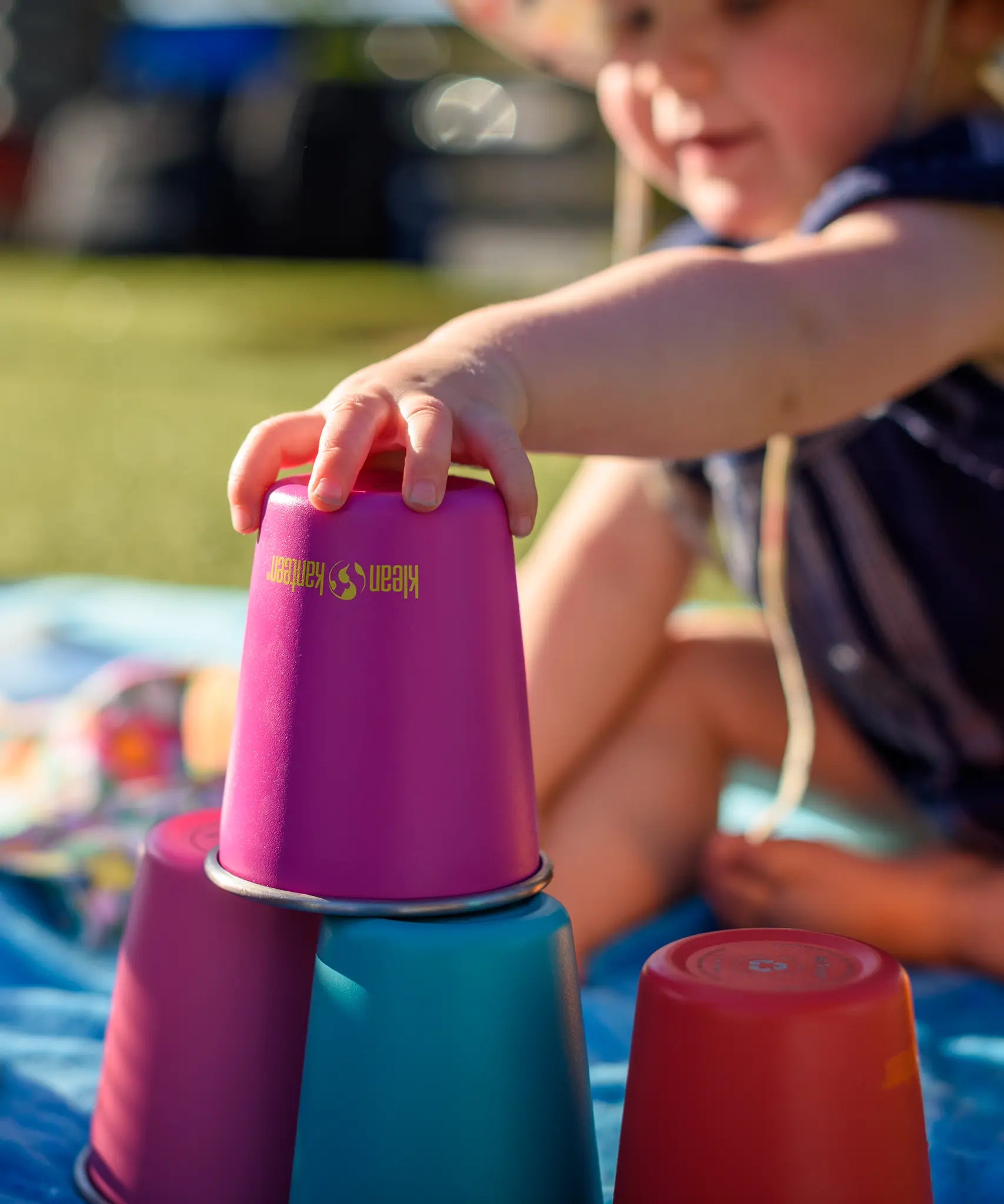 Child stacking the Klean Kanteen stainless steel kid cups in the gum drops colour way on top of each other. 