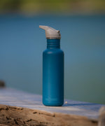Blue Klean Kanteen bottle fitted with a taupe Flip Seal Sports Cap photographed beside water outdoors