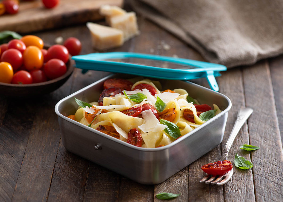 Klean Kanteen 20oz food box filled with tomato and cheese pasta on a wooden worktop next to a bowl of tomatoes and a fork