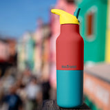 Klean Kanteen Rise Insulated Classic Bottle with Flip Seal Cap in limited edition Cayenne colourway with a colourful seaside town background.