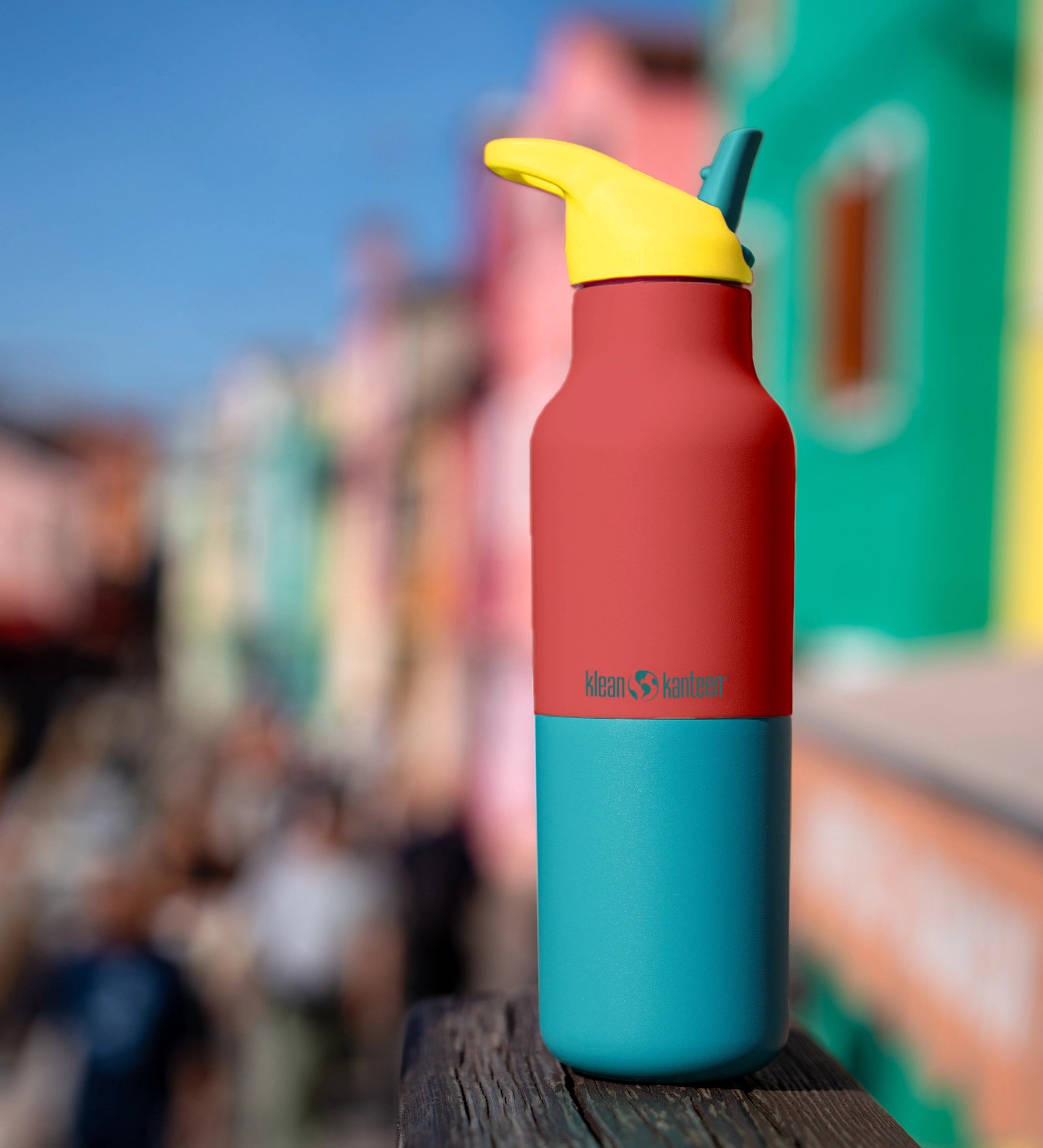 Klean Kanteen Rise Insulated Classic Bottle with Flip Seal Cap in limited edition Cayenne colourway with a colourful seaside town background.