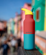 Klean Kanteen Rise Insulated Classic Bottle with Flip Seal Cap in limited edition Cayenne colourway with a colourful seaside town background.