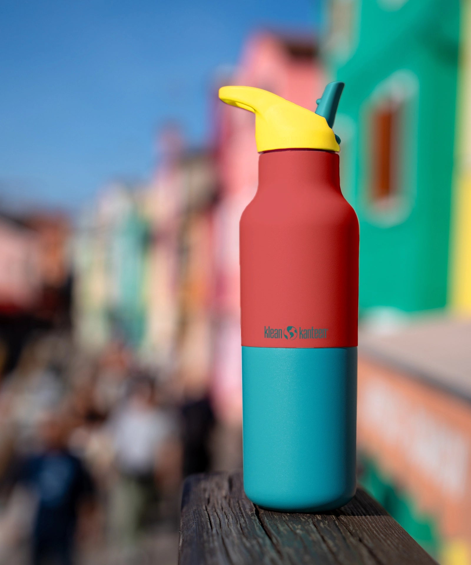 Klean Kanteen Rise Insulated Classic Bottle with Flip Seal Cap in limited edition Cayenne colourway with a colourful seaside town background.