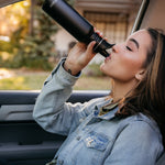 Woman sat in a car drinking from a Klean Kanteen stainless steel drinks bottle with a sports lid