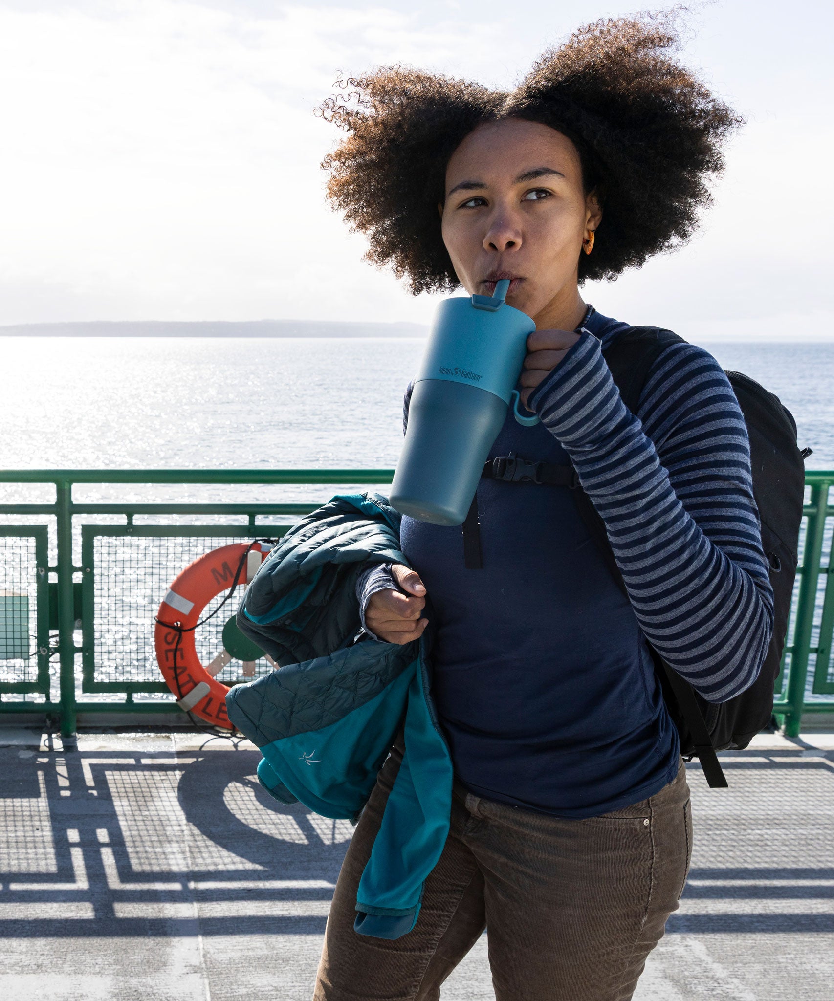 A woman sipping the straw on the brittany blue coloured 26oz Klean Kanteen rise tumbler. 