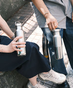 2 adults holding the   klean Kanteen reflect stainless steel rise bottles showing their scale and handle detail on the loop cap