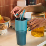 A close up of an adult's hands holding the Brittany Blue colourway Klean Kanteen handled, insulated Rise Tumbler in 26oz, preparing a drink on a kitchen work surface. 