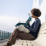 A woman sitting on a white bench sipping the straw on a brittany blue coloured 26oz Klean Kanteen rise handled tumbler. 