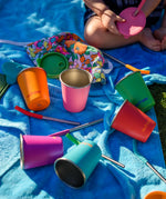 Six colours of Klean Kanteen 10oz/296ml Steel Kid Cups with Straw Lids taken off and straws taken out placed on a blue blanket.