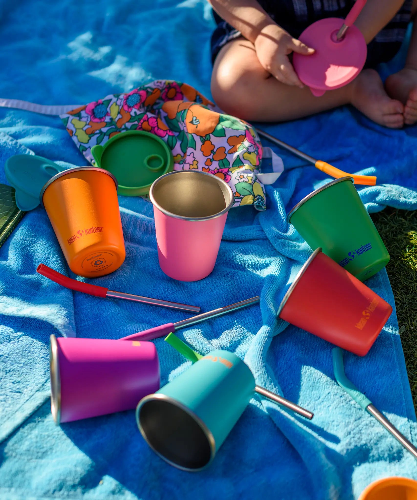 Six colours of Klean Kanteen 10oz/296ml Steel Kid Cups with Straw Lids taken off and straws taken out placed on a blue blanket.