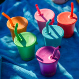 Six colours of Klean Kanteen 10oz/296ml Steel Kid Cups with Straw Lids placed on a blue blanket.