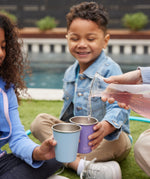 Children holding Klean Kanteen Steel Kid Cups, an adult can be seen pouring raspberry lemonade into the cups. 