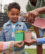 Children holding Klean Kanteen Steel Kid Cups, an adult can be seen pouring raspberry lemonade into the cups. 