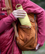 Adult packing a wax yellow Klean Kanteen 20oz insulated bottle with matching lid in a side pocket on a backpack