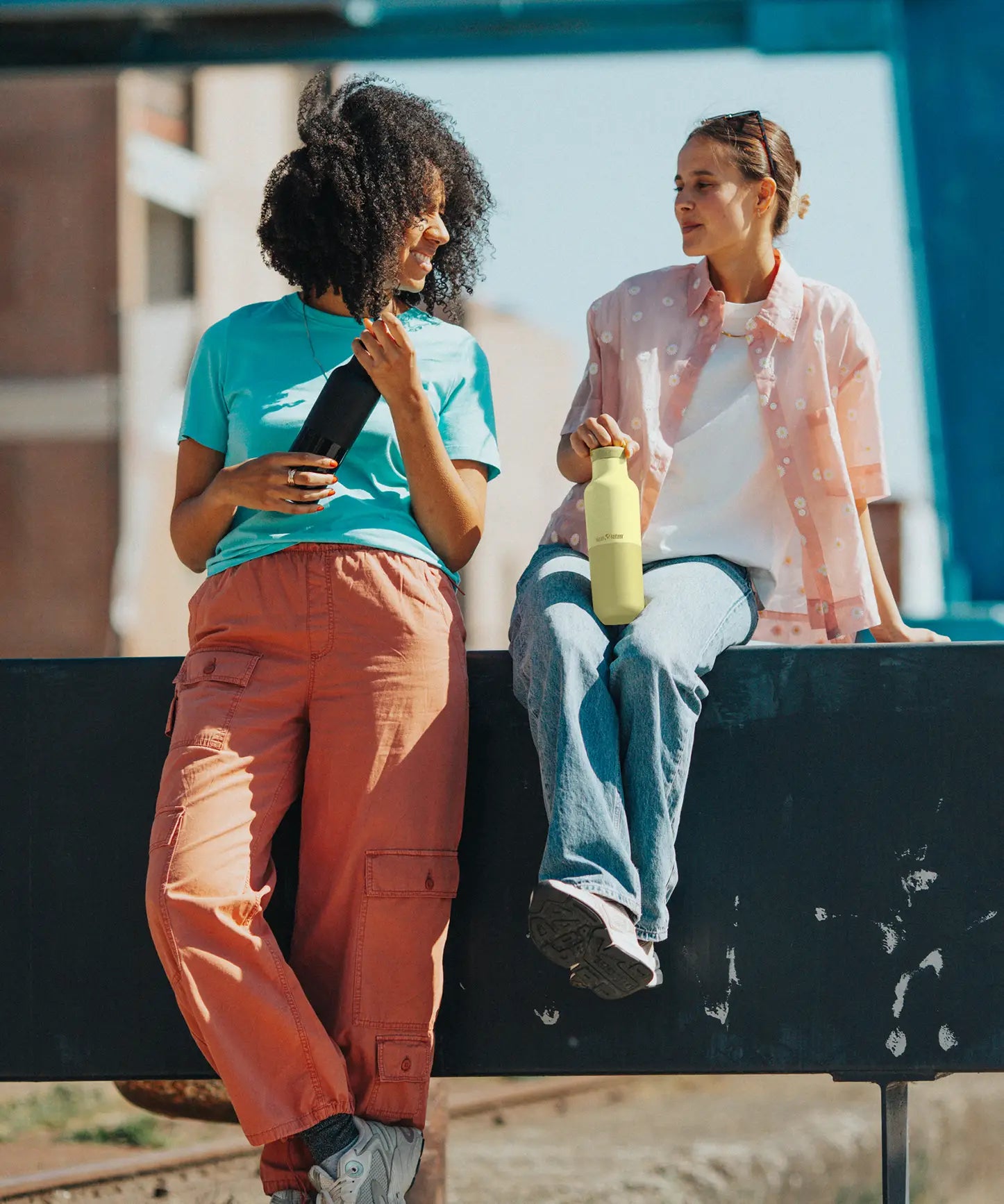 Adult holding a wax yellow Klean Kanteen 20oz insulated bottle with matching lid next to an adult holding a black bottle