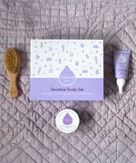 A top down image of the products included with the sensitive gift set next to the packaging showing the scalp cream, natural baby brush and and organic coconut oil available at Babipur.