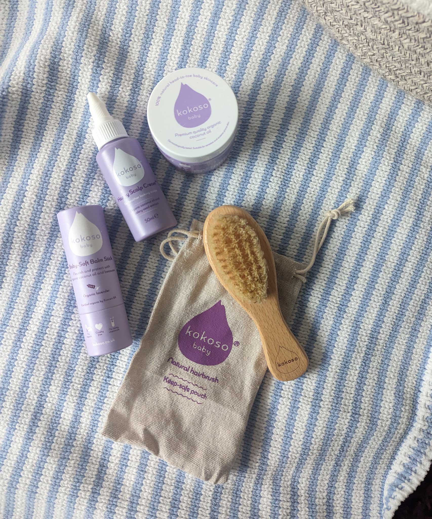 A collection of Kokoso baby crae items including the Happy Scalp Cream in a 50ml container, small tub of organic coconut oil, hairbrush and baby soft balm stick. The Kokoso baby care range is available at Babipur.