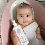 A child sat in a baby bath with a person holding the Kokoso Fragrance Free Hair and Body Wash bottle next to them