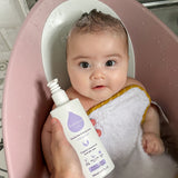 A child sat in a baby bath with a person holding the Kokoso Fragrance Free Hair and Body Wash bottle next to them