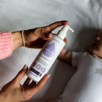 Close up of a woman's hands holding the Kokoso fragrance-free coconut oil lotion above a baby laying on a white bed
