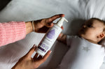 Close up of a woman's hands holding the Kokoso fragrance-free coconut oil lotion above a baby laying on a white bed