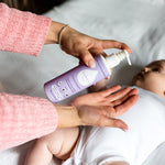 Close up of woman's hand pumping the Kokoso organic coconut baby oil lotion into her hand above a baby