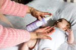 Close up of woman's hand pumping the Kokoso organic coconut baby oil lotion into her hand above a baby