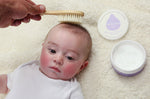 Close up of baby laying on a white fluffy background having its hair brushed with the Kokoso natural wooden hairbrush