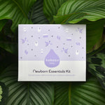 The reverse of the Kokoso Newborn Essentials Organic Baby Gift Set in its purple and white gift box sitting on a backdrop of large Green leaves. The words "Pure and gentle skincare for brand new babies" stand out.