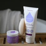 Kokoso Newborn Essentials Organic Baby Gift Set in its purple and white gift box sitting on a backdrop of large Green leaves