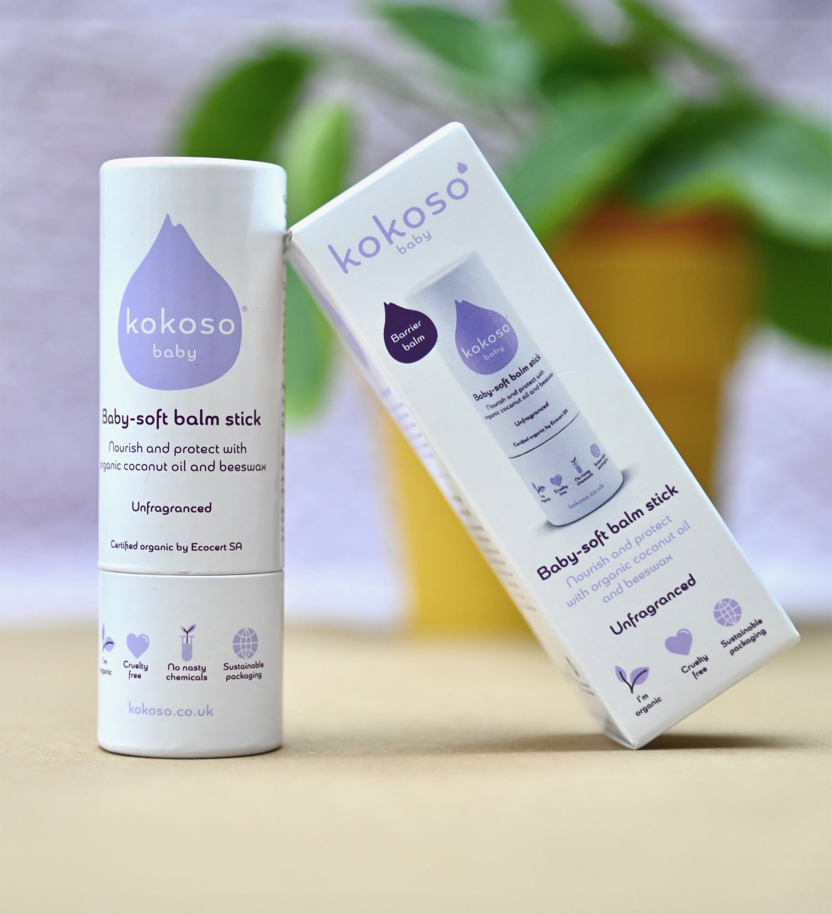 Kokoso unfragranced baby soft balm stick available at Babipur. with a blurred plant in the background.