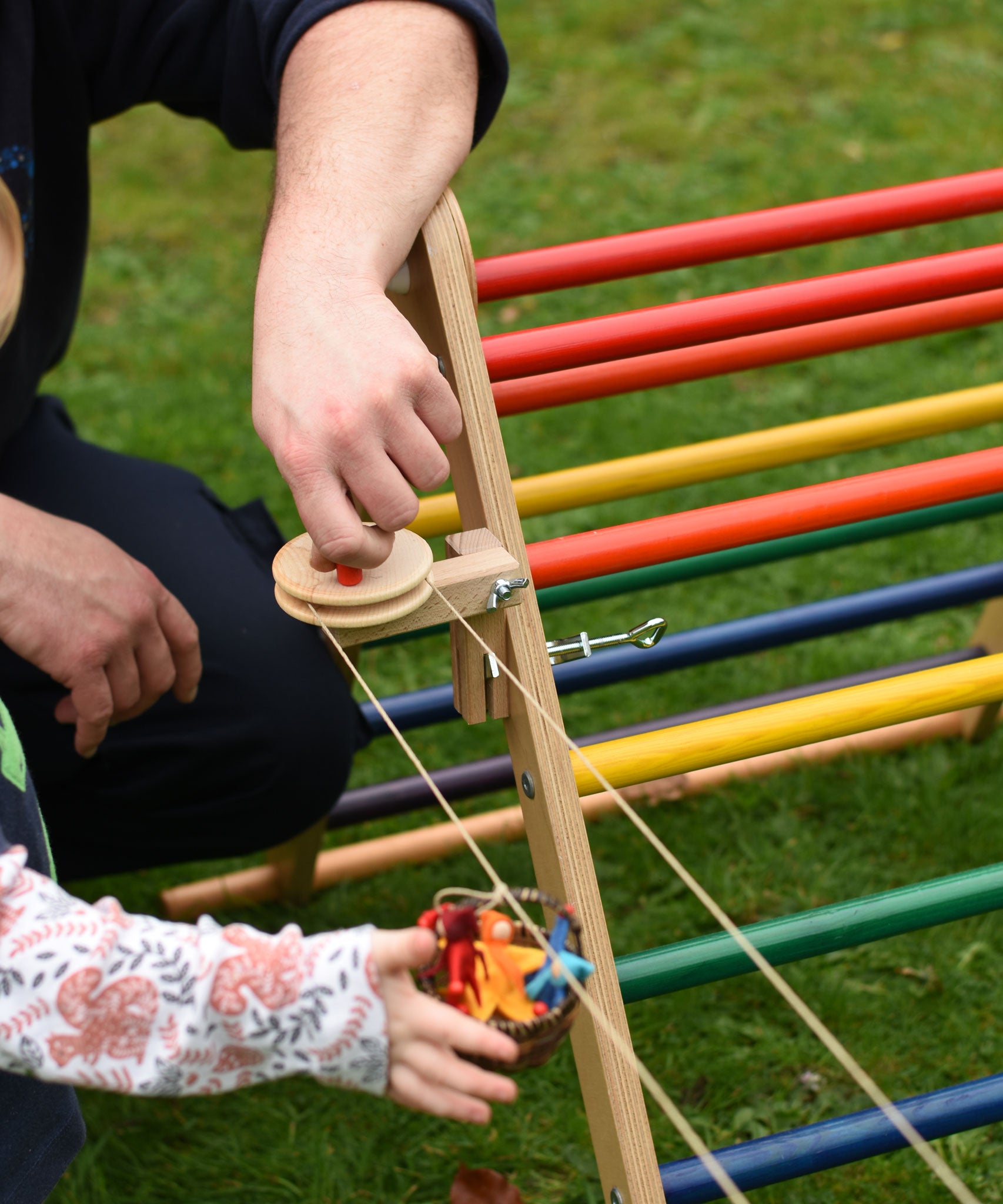 The Kraul DIY Basket Cable Car STEM Kit set up outdoors attached to a TriClimb.  An adult's hand can be seen turning the wheel control in the background. 