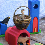 A Bumbu heron placed in a large Kraul basket placed on a wooden Glucksakfer castle in a small world play scene.