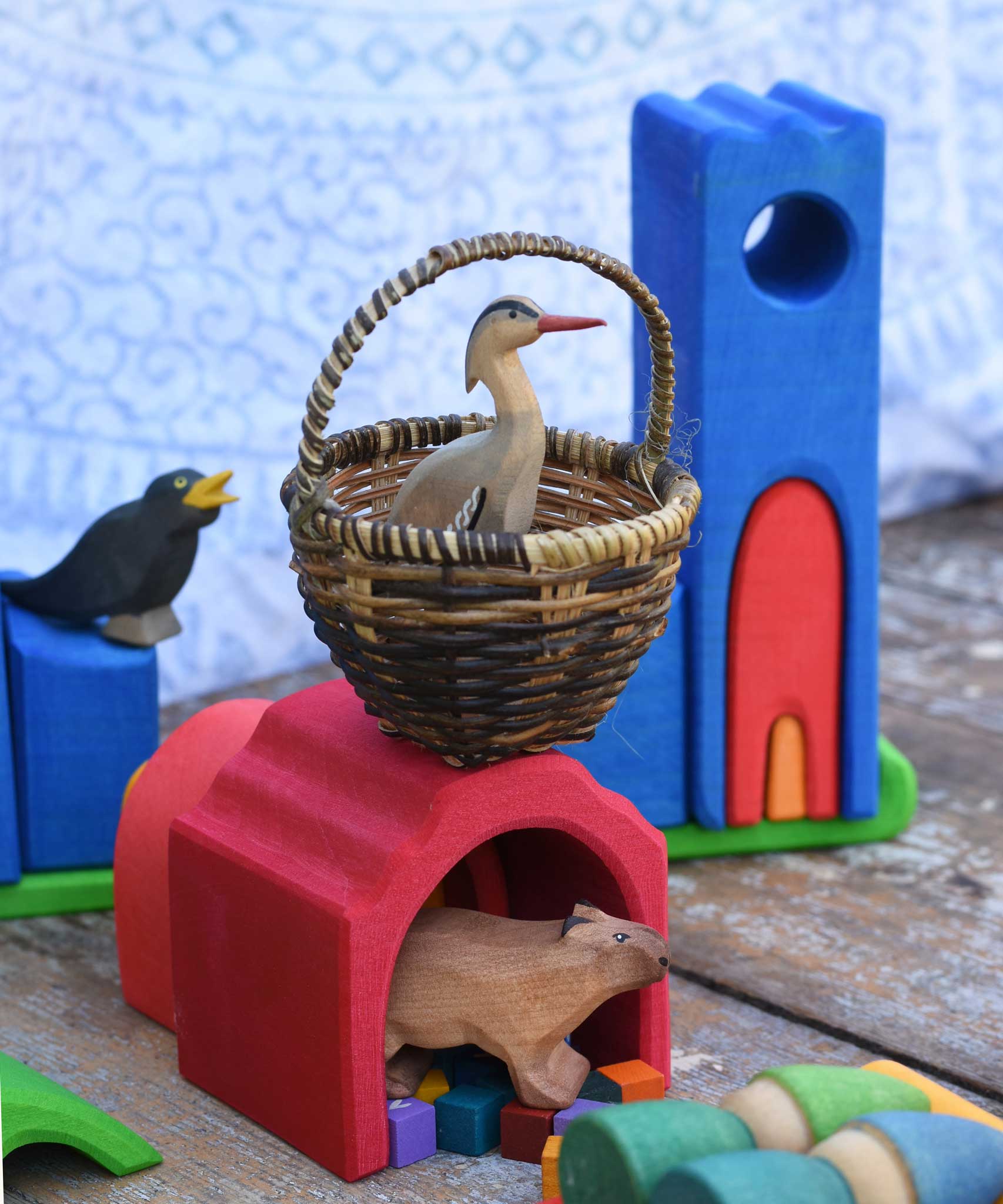 A Bumbu heron placed in a large Kraul basket placed on a wooden Glucksakfer castle in a small world play scene.