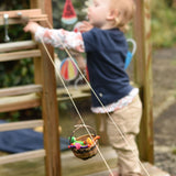 A wicker basket travelling along on the rope of the Kraul DIY Basket Cable Car STEM Kit.  A child can be seen reaching for the control wheel in the background