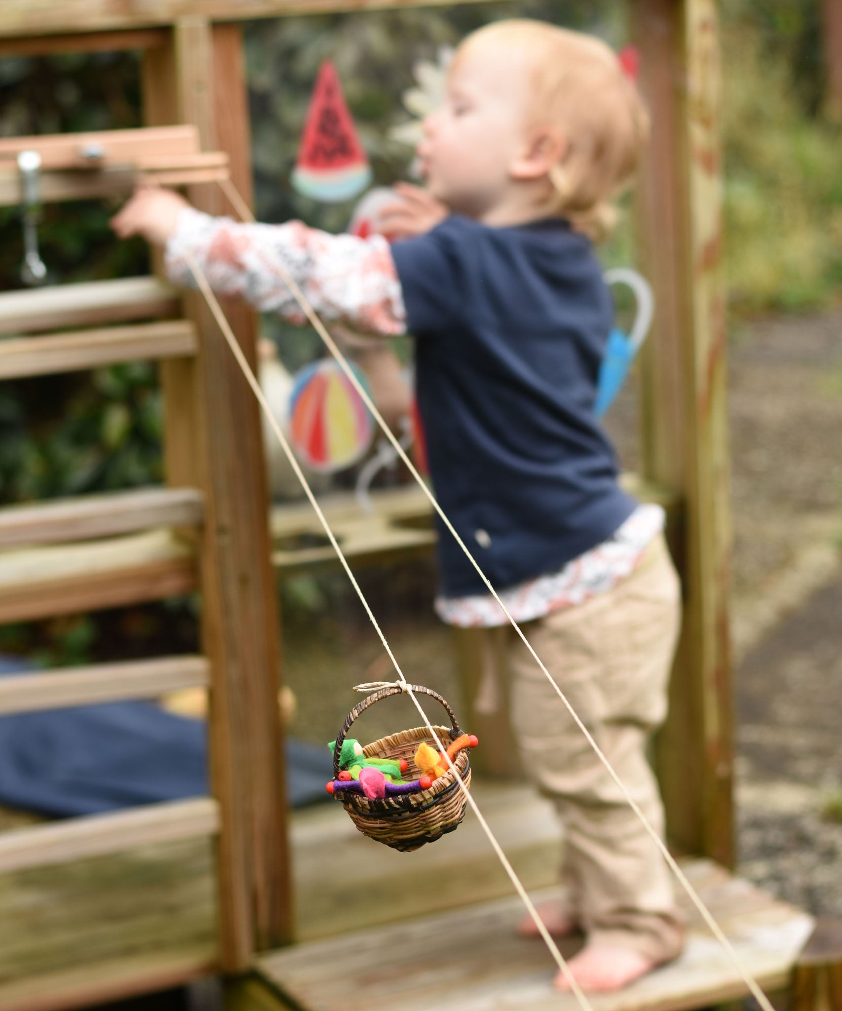 A wicker basket travelling along on the rope of the Kraul DIY Basket Cable Car STEM Kit.  A child can be seen reaching for the control wheel in the background
