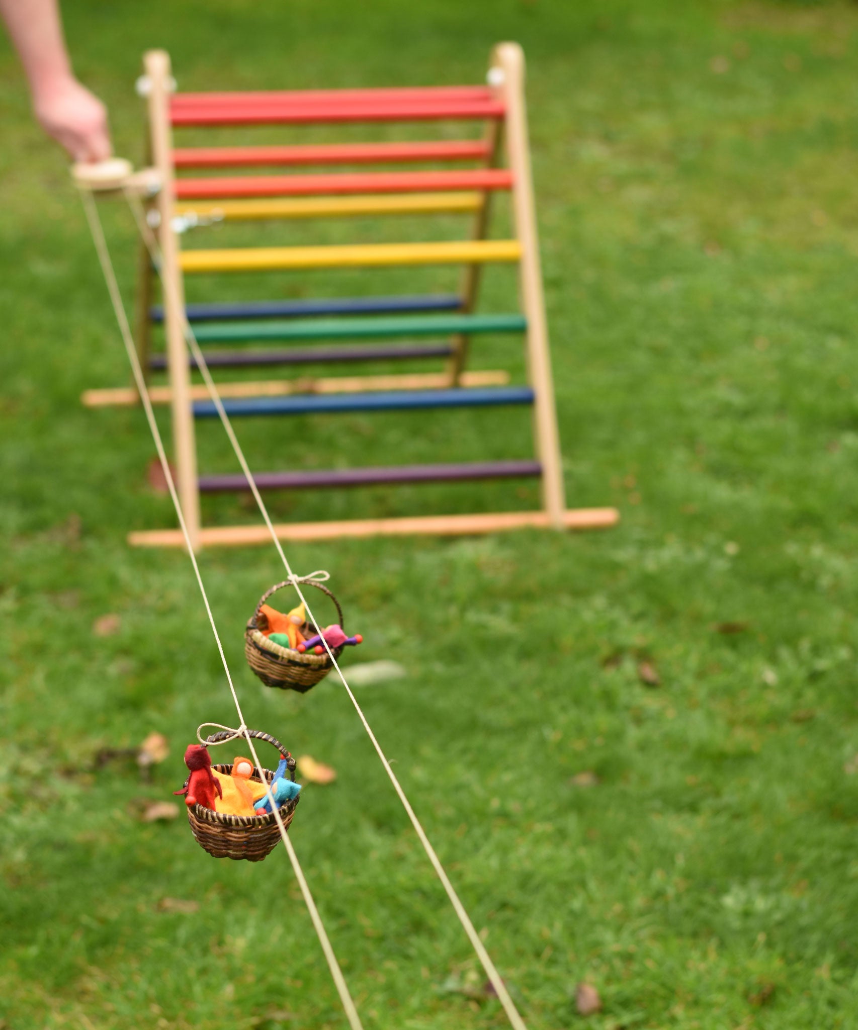 Two wicker baskets travelling along on the rope of the Kraul DIY Basket Cable Car STEM Kit.  An adult's hand can be seen turning the wheel control in the background. 