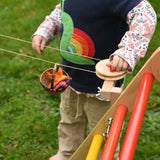 A close up of a child's hand turning the wheel of the Kraul DIY Basket Cable Car STEM Kit as a basket filled with felt passenger moves along the string.