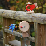 A blue Kraul felt passenger doll placed on the string of the Kraul DIY Basket Cable Car STEM Kit. A Bajo fire engine helicopter can bee seen nearby.  