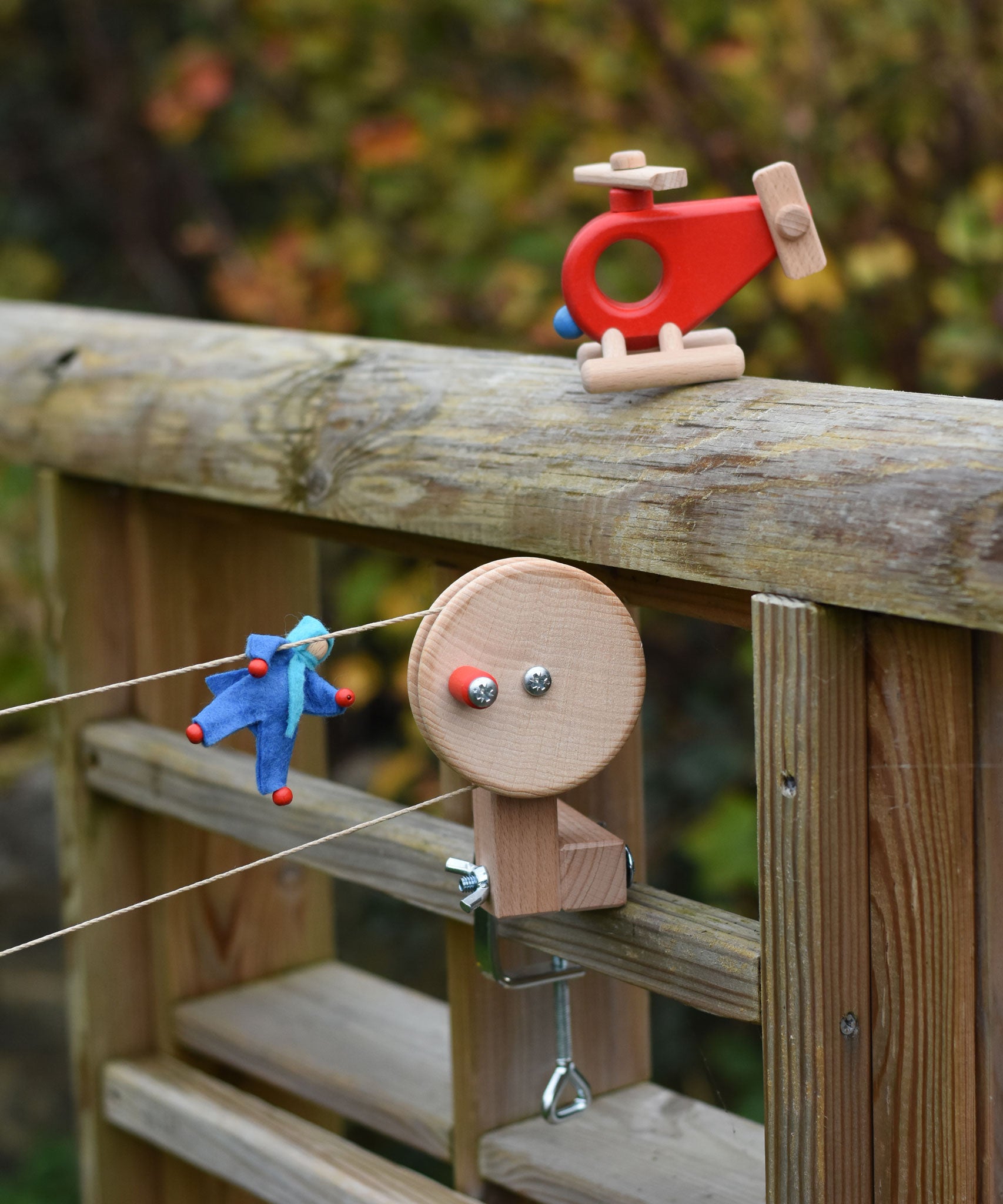 A blue Kraul felt passenger doll placed on the string of the Kraul DIY Basket Cable Car STEM Kit. A Bajo fire engine helicopter can bee seen nearby.  