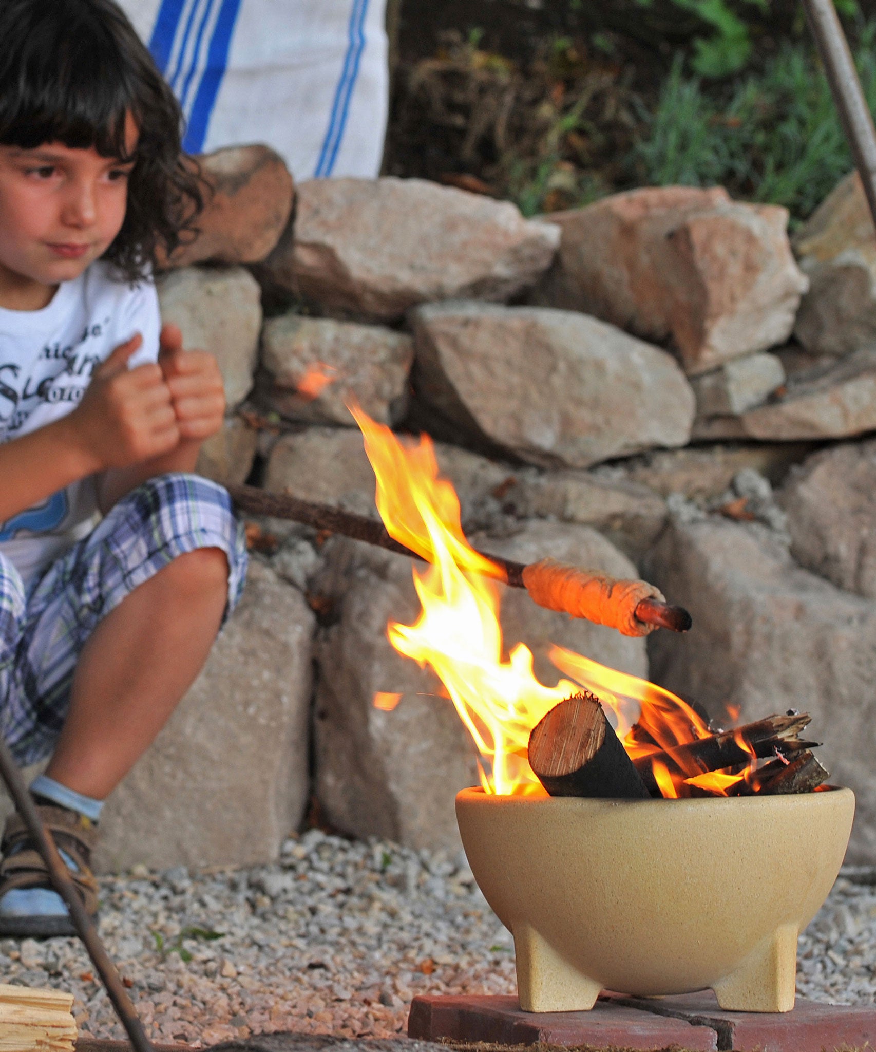 A child sitting by a fire lit in the Kraul children's ceramic fire bowl. Kraul is available at Babipur their range of kits let children discover a world of wonder with Kraul STEM science kits and educational toys.