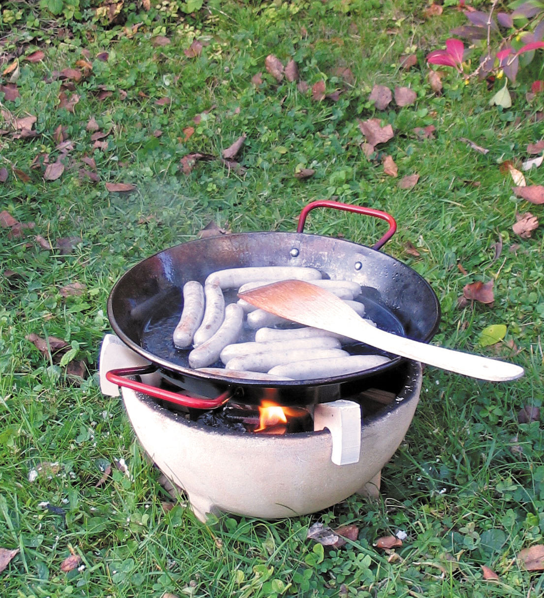 Sausages placed in a Kraul cooking pan that has been placed on a lit fire in the Kraul ceramic fire bowl. Kraul is available at Babipur their range of kits let children discover a world of wonder with Kraul STEM science kits and educational toys.