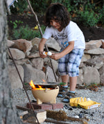 A child breaking an egg into the Kraul Cooking pan that has been placed on a lit fire in the Kraul ceramic fire bowl.  Kraul is available at Babipur their range of kits let children discover a world of wonder with Kraul STEM science kits and educational toys.
