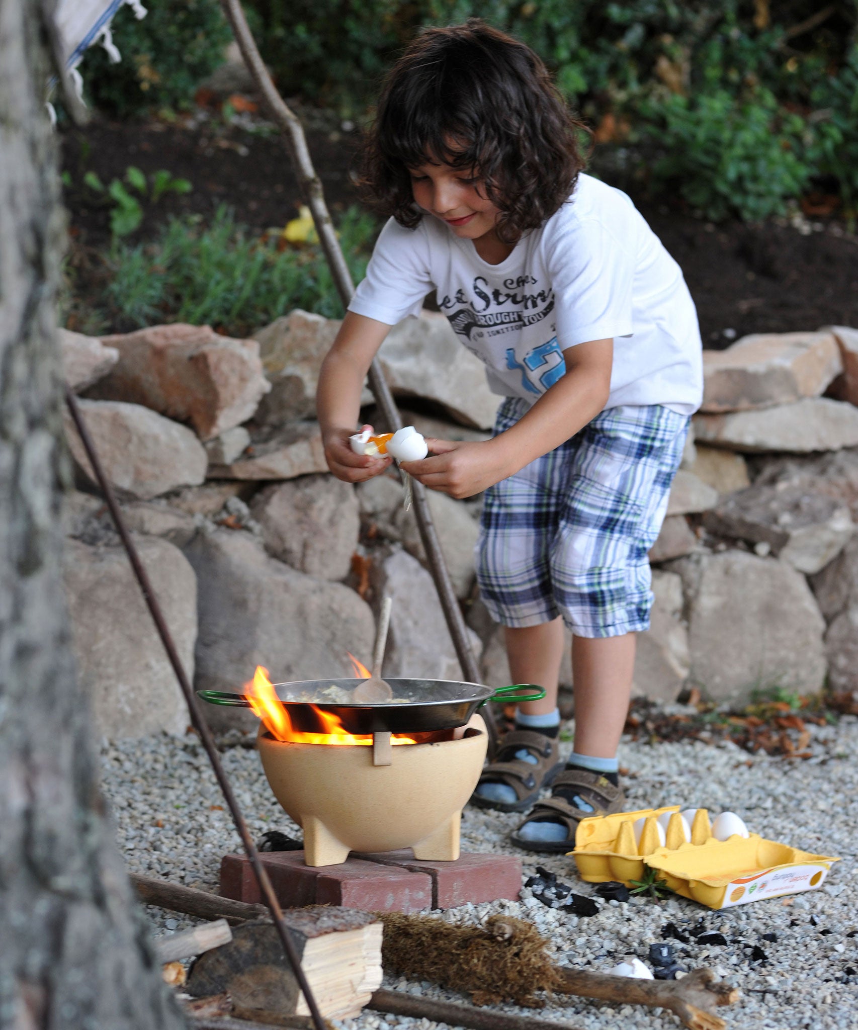 A child breaking an egg into the Kraul Cooking pan that has been placed on a lit fire in the Kraul ceramic fire bowl.  Kraul is available at Babipur their range of kits let children discover a world of wonder with Kraul STEM science kits and educational toys.