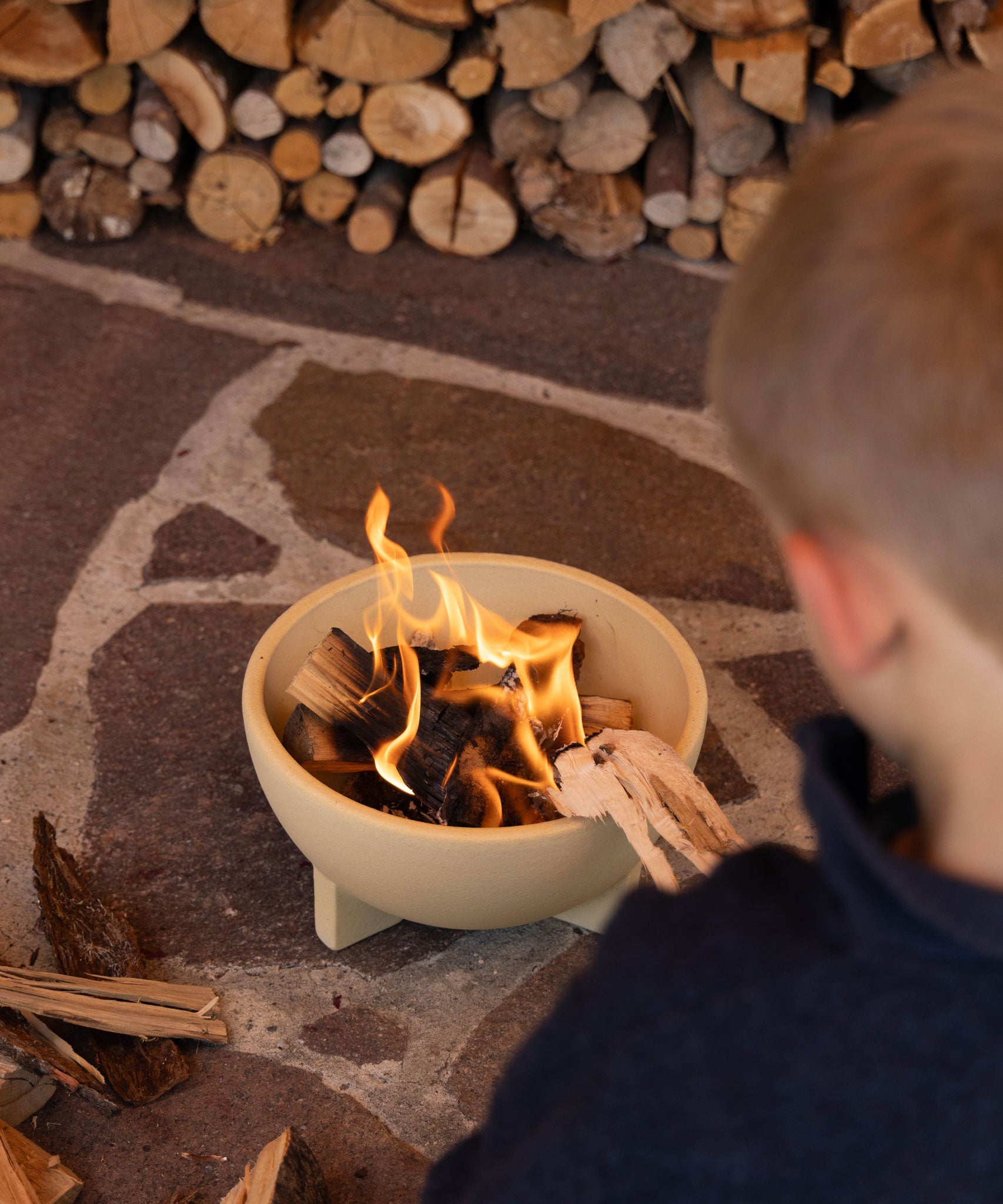 A child sitting by a fire lit in the Kraul children's ceramic fire bowl. Kraul is available at Babipur their range of kits let children discover a world of wonder with Kraul STEM science kits and educational toys.