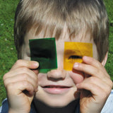 Child holding a green and yellow Kraul colour slide near the eyes showing their transparency.